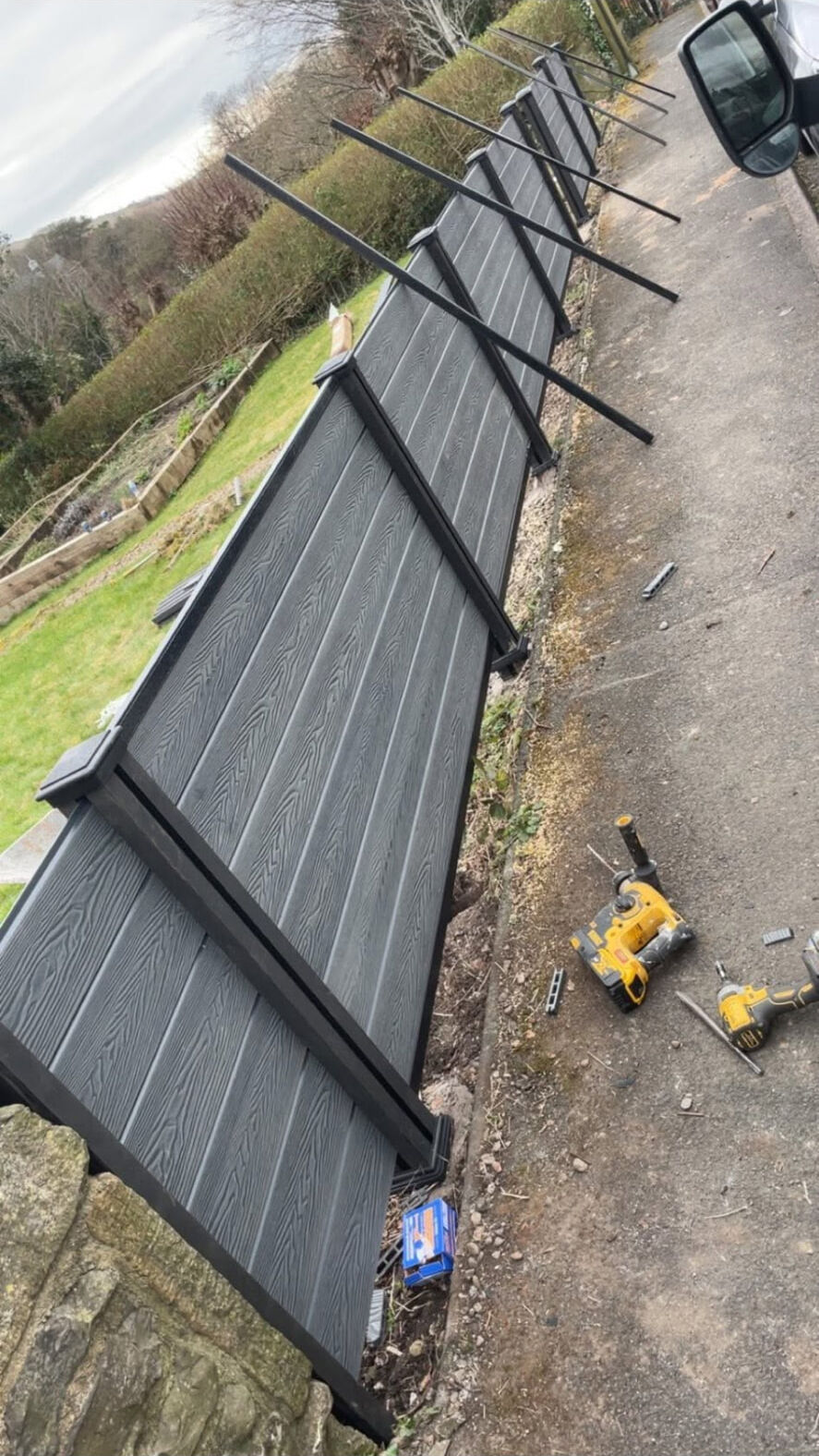 Grey wood-effect fence panels being installed along a roadside with temporary bracing
