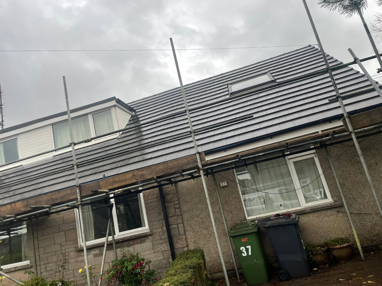 Tiled roof with roof window and scaffolding erected along the front of a house